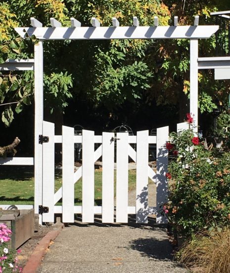 White arbor with gate, entry to back yard